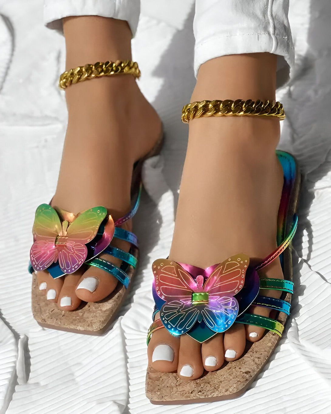 Une image de pieds avec des sandales plates à talons compensés en liège. Les sandales sont décorées de papillons multicolores. Les pieds sont sur un tapis blanc.