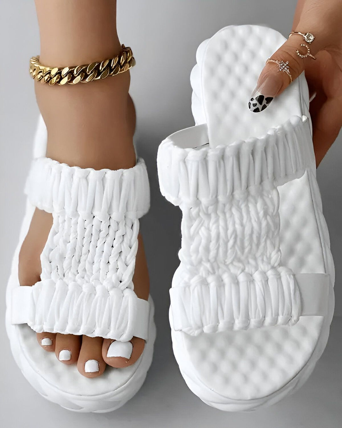 Une paire de sandales blanches pour femme. Les sandales sont en matière synthétique et ont une semelle compensée. Elles sont dotées de deux brides qui passent sur le dessus du pied et d'une bride qui passe entre les orteils. Les sandales sont fermées par une boucle sur le côté.