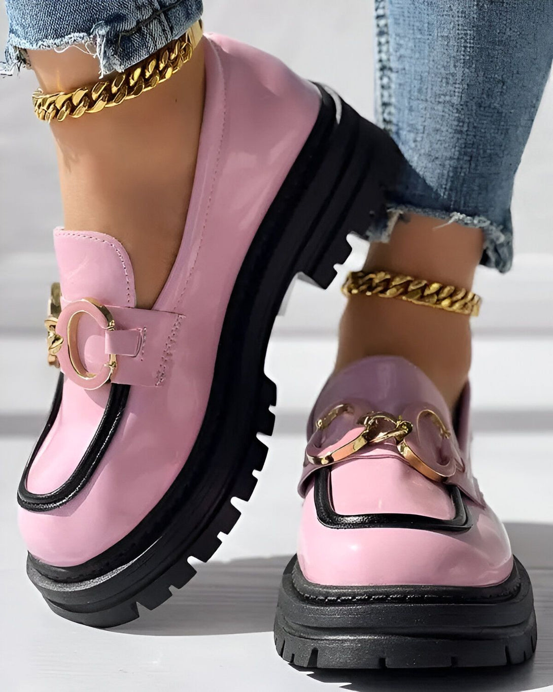 Une paire de chaussures roses et noires avec un fermoir doré. Les chaussures sont portées par une femme qui porte un jean bleu et des chaussettes blanches.