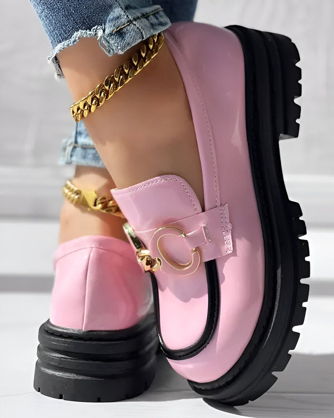Une femme porte des mocassins roses avec un C doré sur le dessus. Elle porte également un jean bleu et un bracelet de cheville doré.