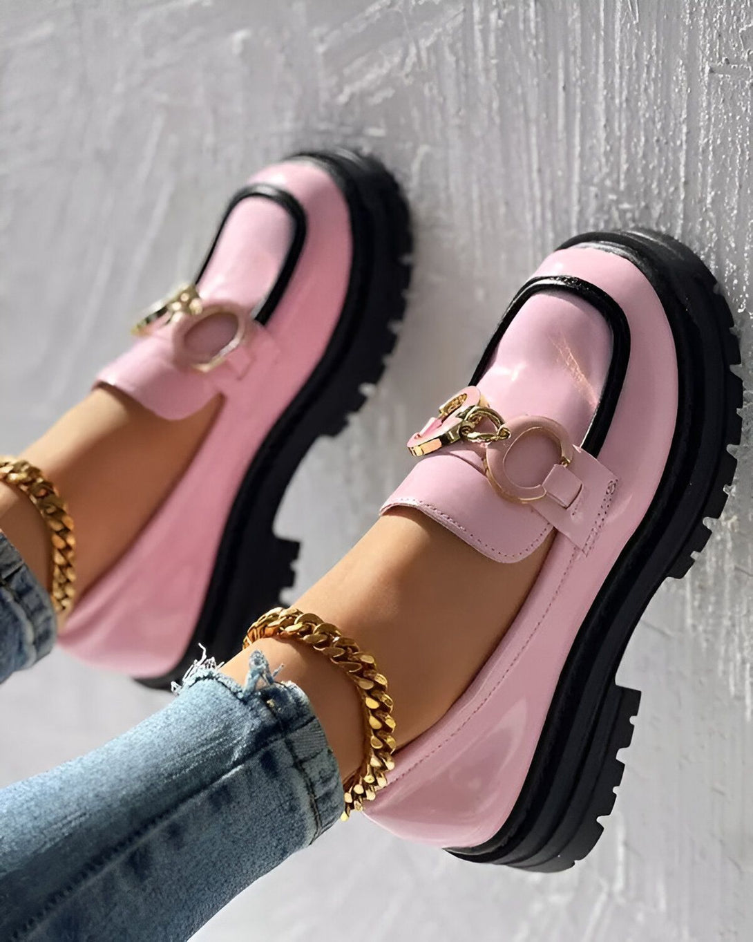 Une paire de chaussures roses et noires avec une grosse semelle et une boucle dorée.