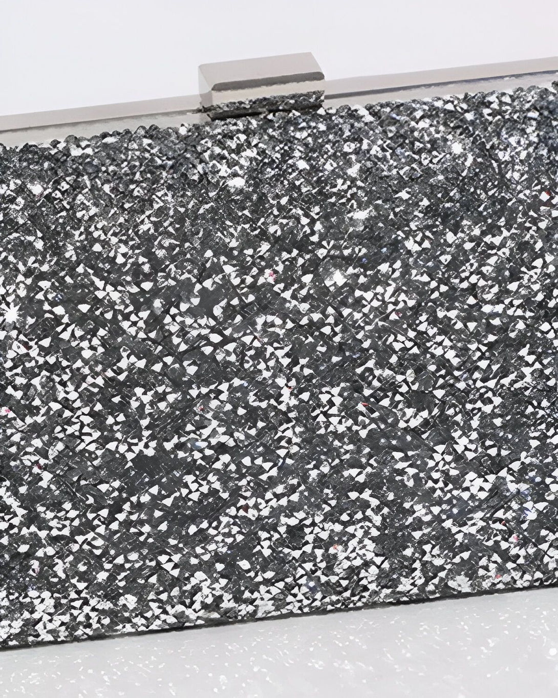 Une image d'une minaudière argentée avec des paillettes et une anse argentée. La minaudière est ouverte et on peut voir l'intérieur qui est en satin noir.