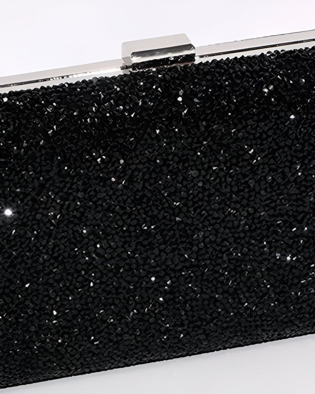 Une image d'une pochette de soirée noire en strass. La pochette est rectangulaire et possède une fermeture argentée. Elle est recouverte de strass noirs qui scintillent à la lumière.