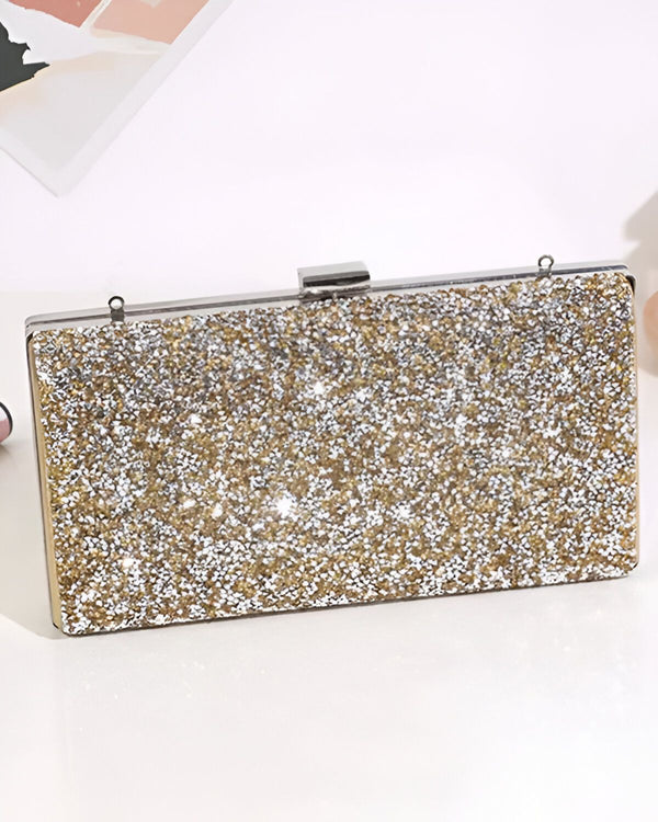 Une image d'une pochette de soirée rigide de couleur or avec une anse argentée. La pochette est recouverte de paillettes et de strass.