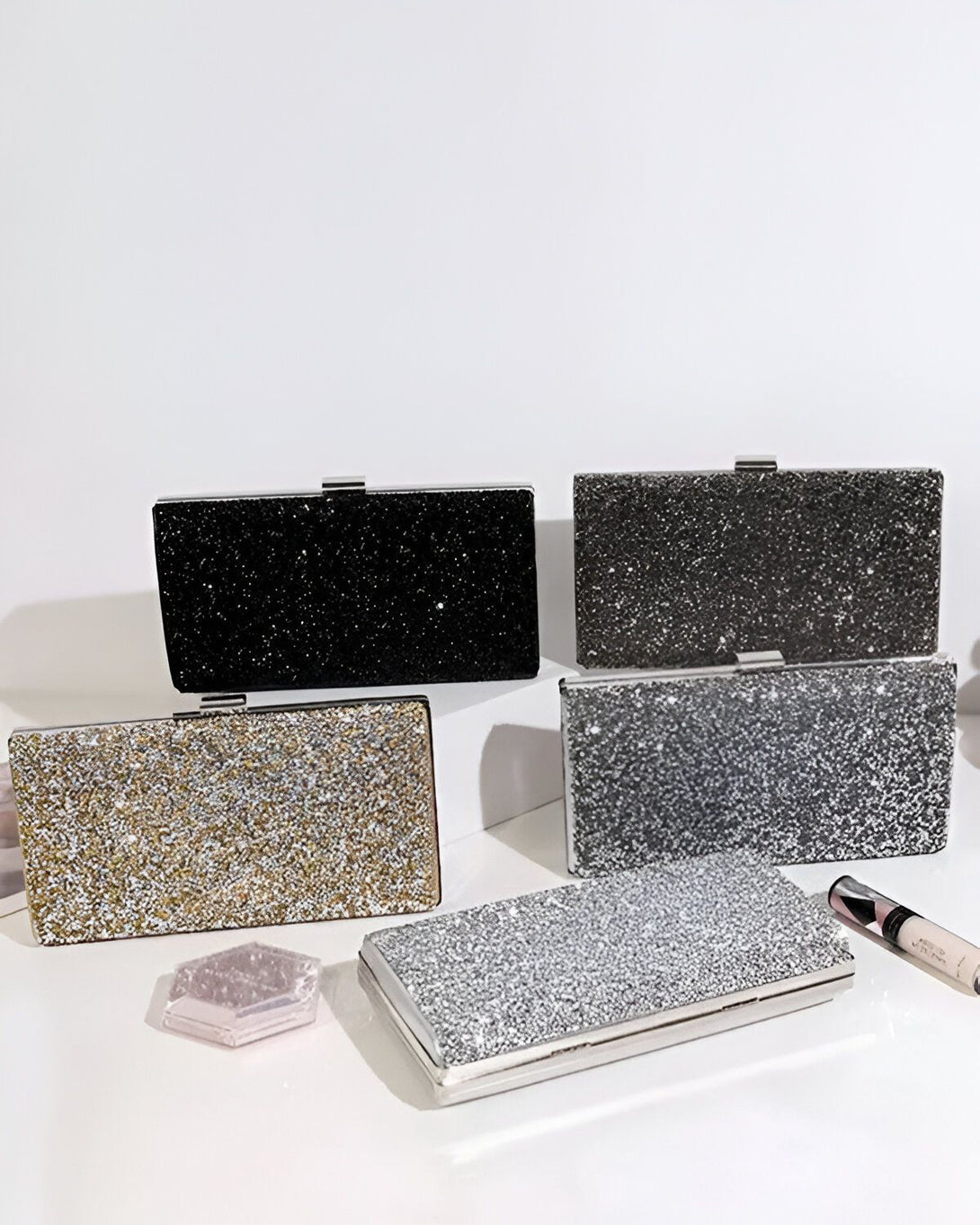 quatre pochettes de soirée rectangulaires à paillettes, de couleur noire, argentée, dorée et grise.