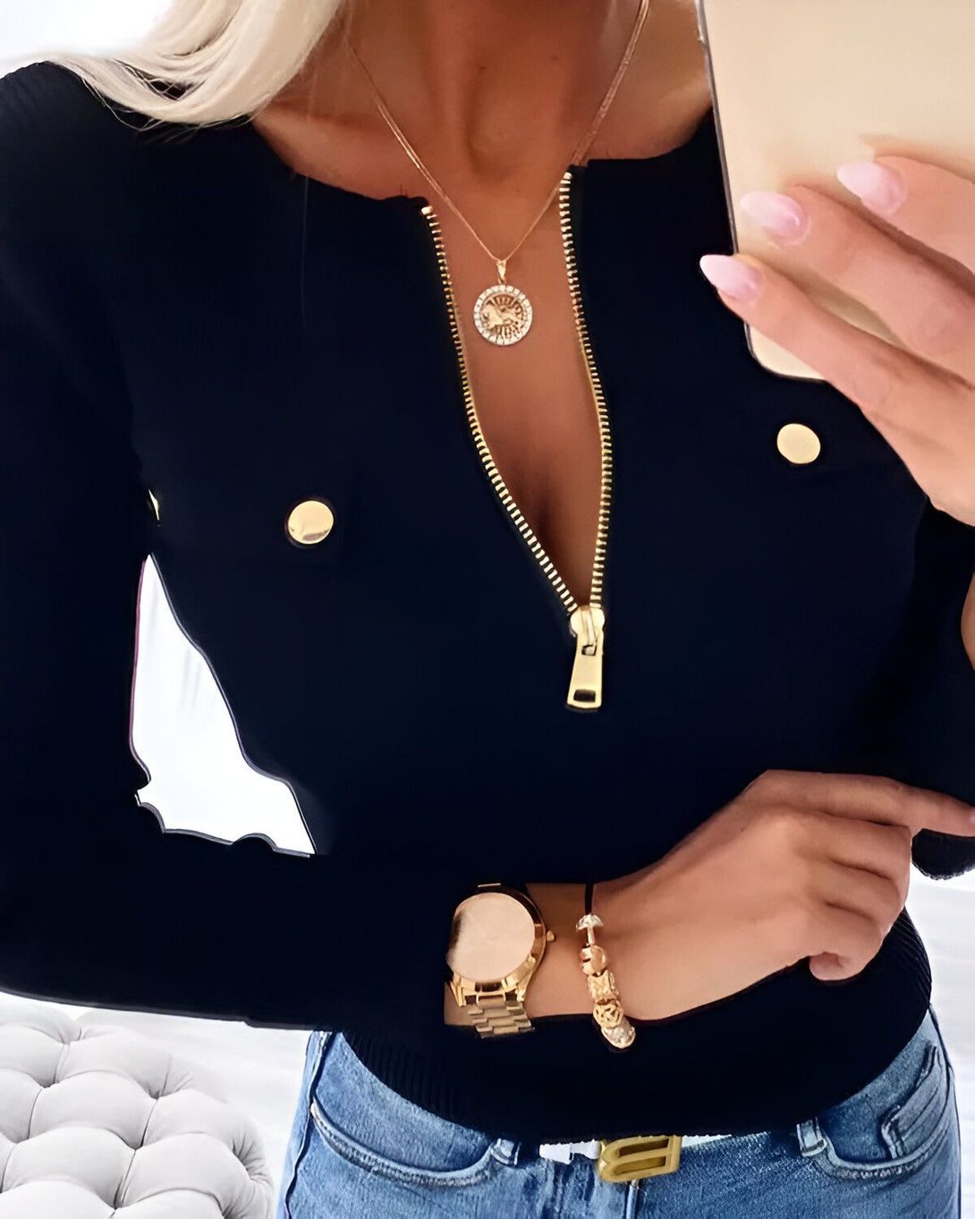 Une femme porte un chemisier noir avec un col zippé et des boutons dorés.