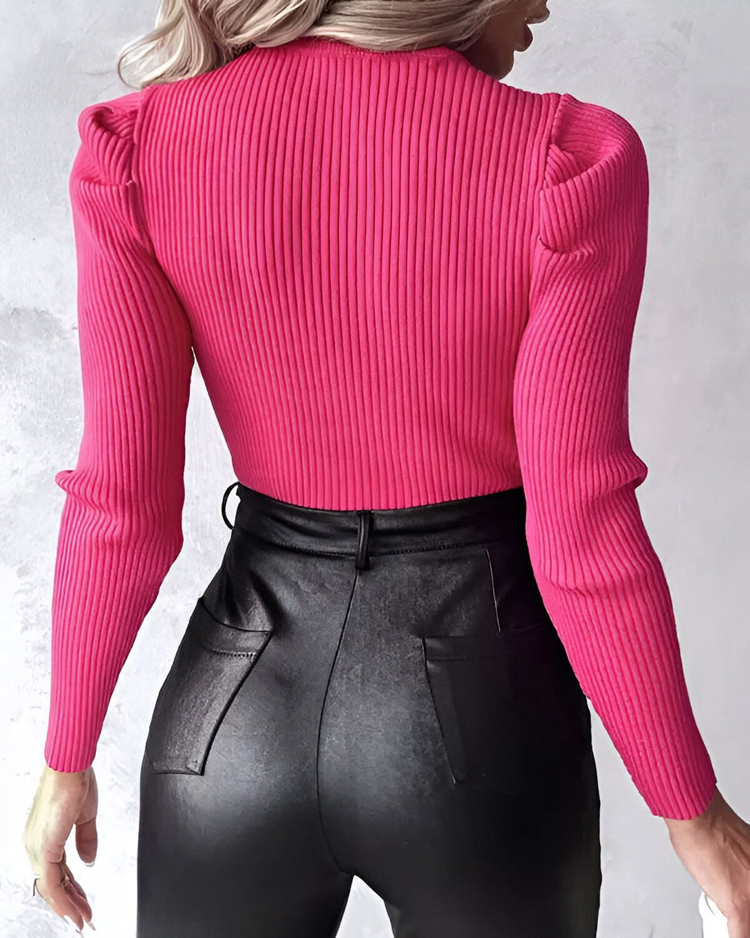 Une femme porte un pull rose à manches bouffantes et un pantalon en cuir noir.