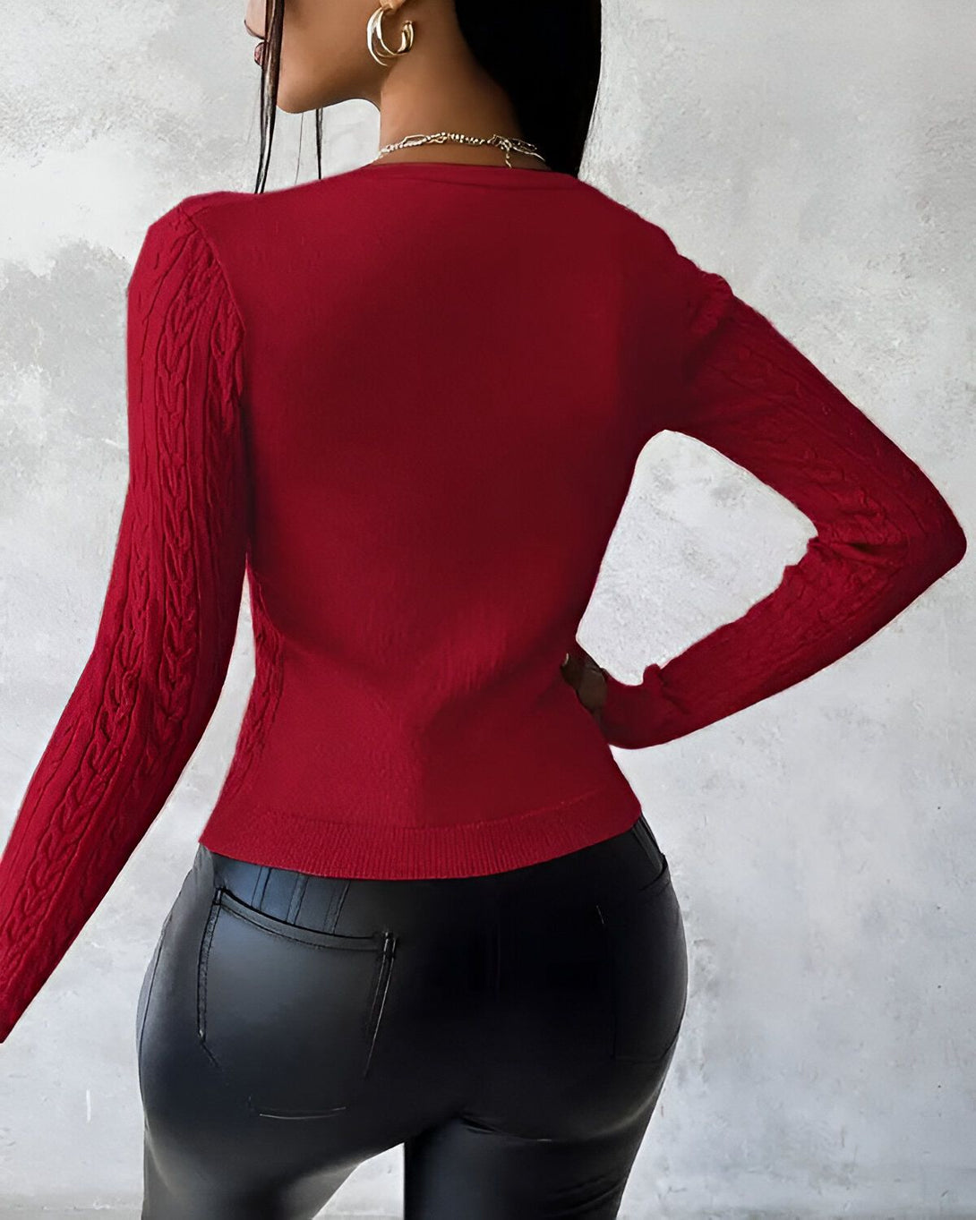 Une femme porte un pull rouge à manches longues et un jean noir.