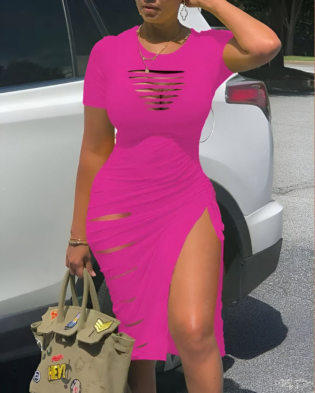 Une femme porte une robe rose moulante avec des fentes sur les côtés et des trous sur le devant. Elle est également porte une veste en jean bleue et des talons hauts noirs.