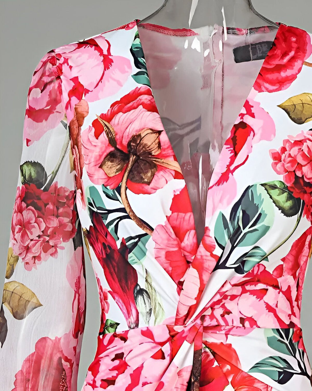 Une robe longue à fleurs avec un décolleté en V et des manches longues. La robe est rose et blanche avec des fleurs rouges et vertes.
