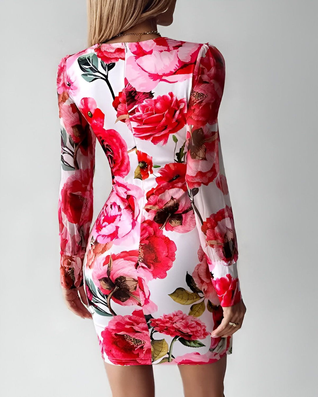 Une femme porte une robe moulante blanche à fleurs roses et rouges. La robe est décolletée et a des manches longues. La femme est vue de dos.
