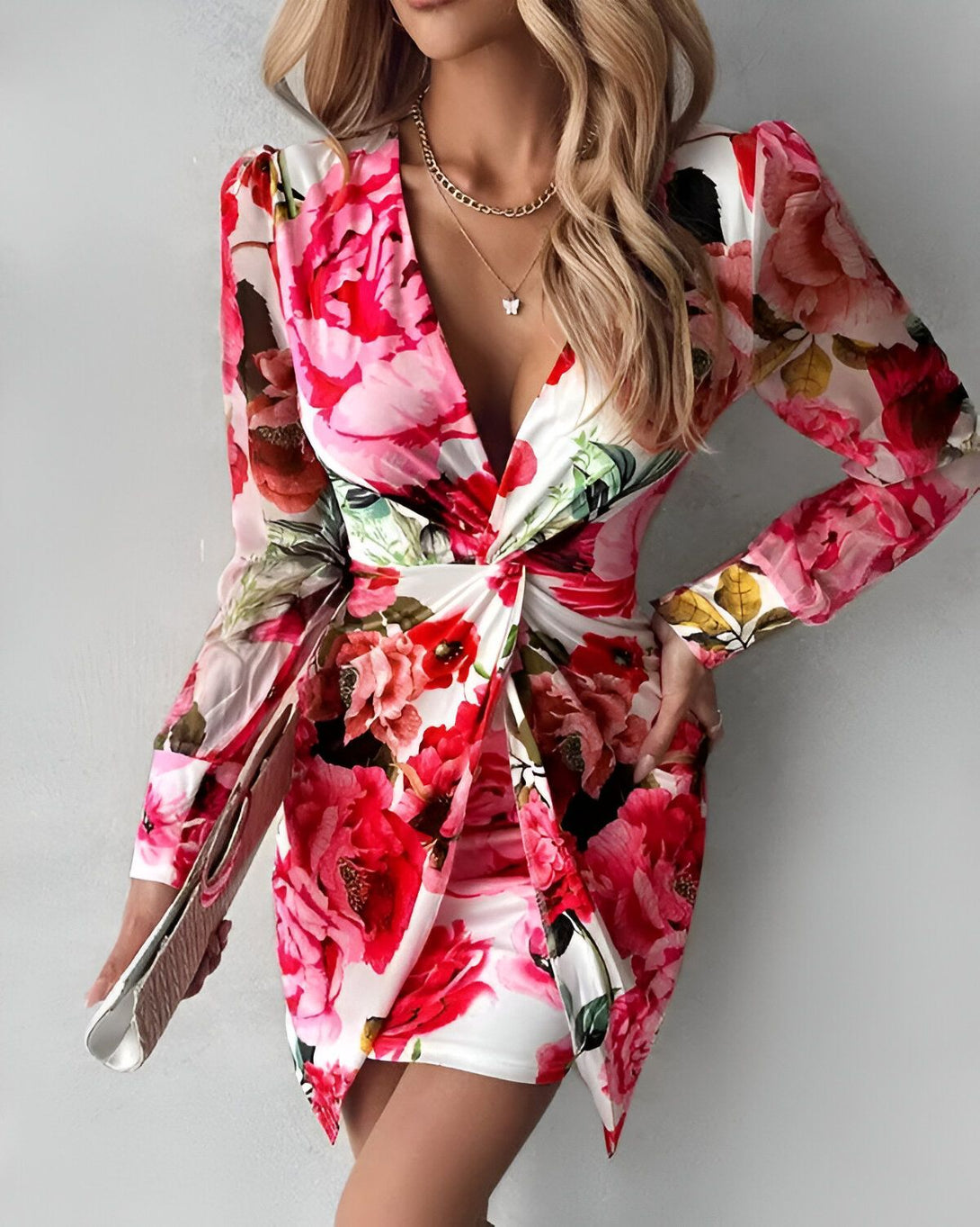 Une femme porte une robe courte à fleurs. La robe est blanche avec des fleurs roses et rouges. La femme a les cheveux blonds et porte un collier.