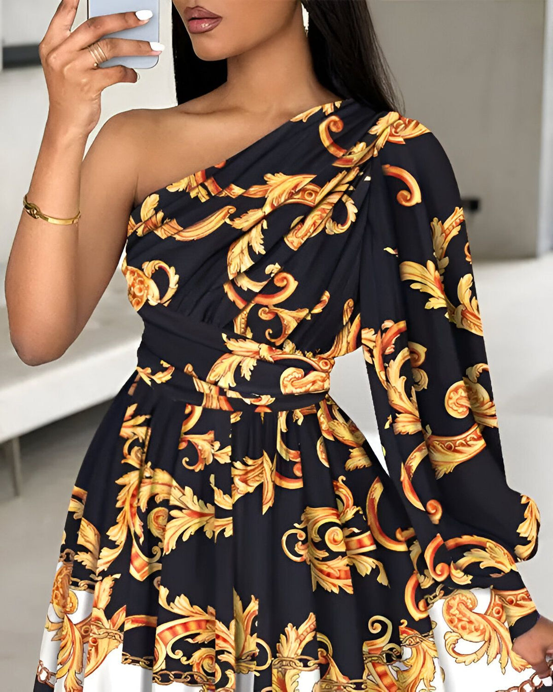 Une femme porte une robe noire et dorée à une épaule. La robe est cintrée à la taille et possède une jupe évasée. La femme est debout, le bras droit levé, tenant un téléphone portable.