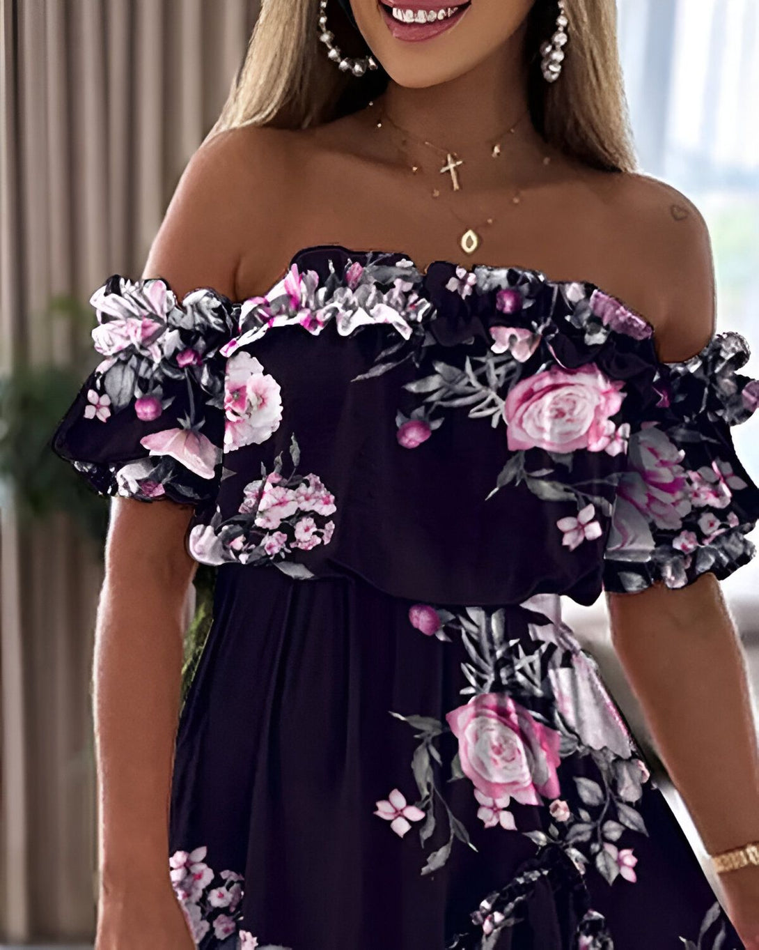 Une jeune femme souriante porte une robe noire à fleurs roses décolletée et épaules dénudées.