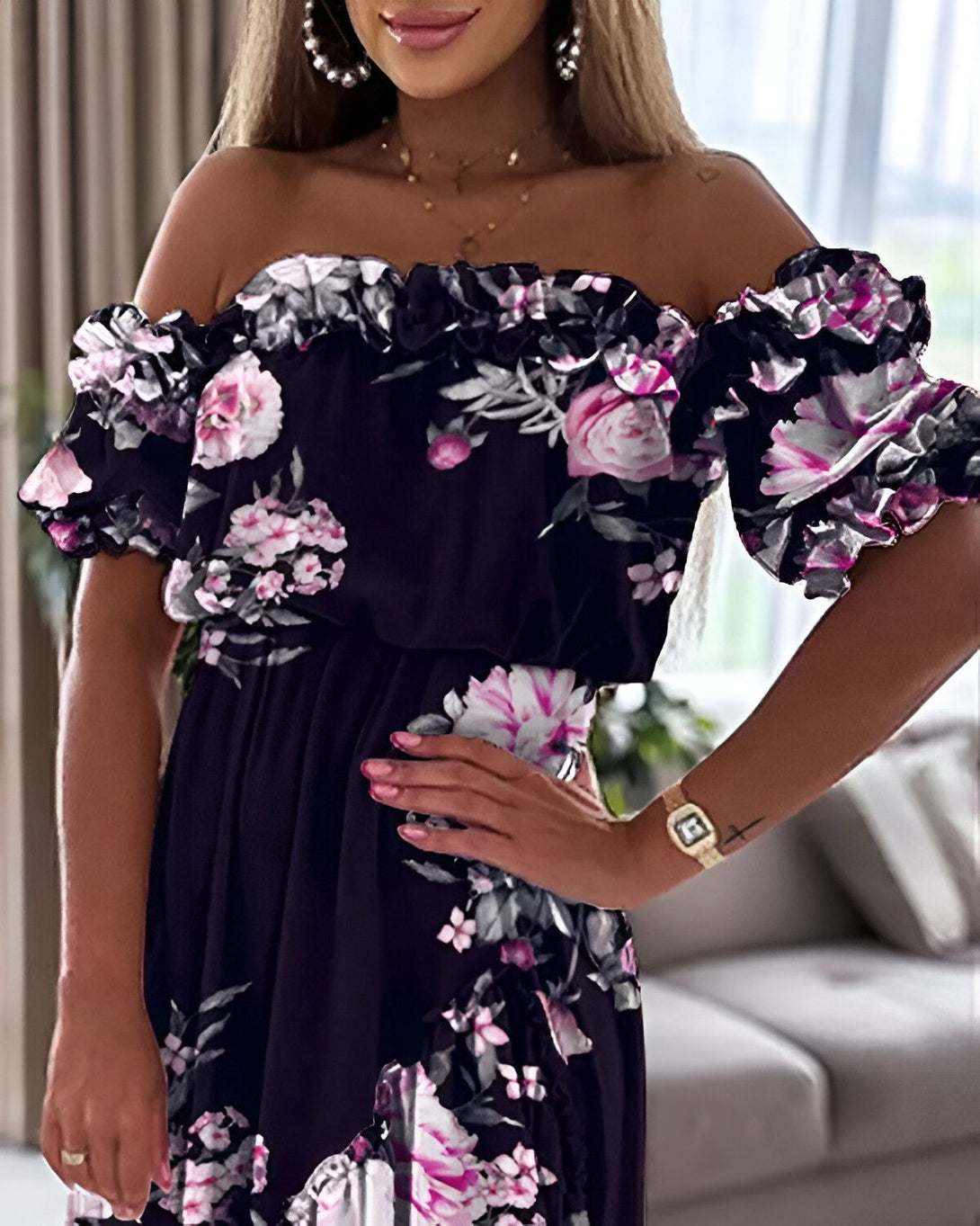 Une femme porte une robe noire à fleurs roses décolletée et volantée.