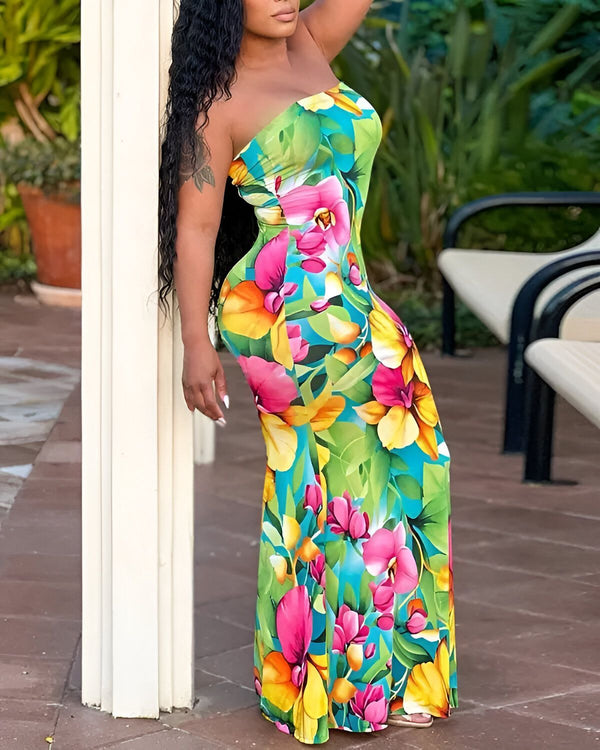 Une femme est debout à côté d'une colonne. Elle porte une robe longue et moulante sans bretelles à motifs de fleurs tropicales multicolores. Ses cheveux sont longs et noirs et elle a un tatouage sur le bras gauche.