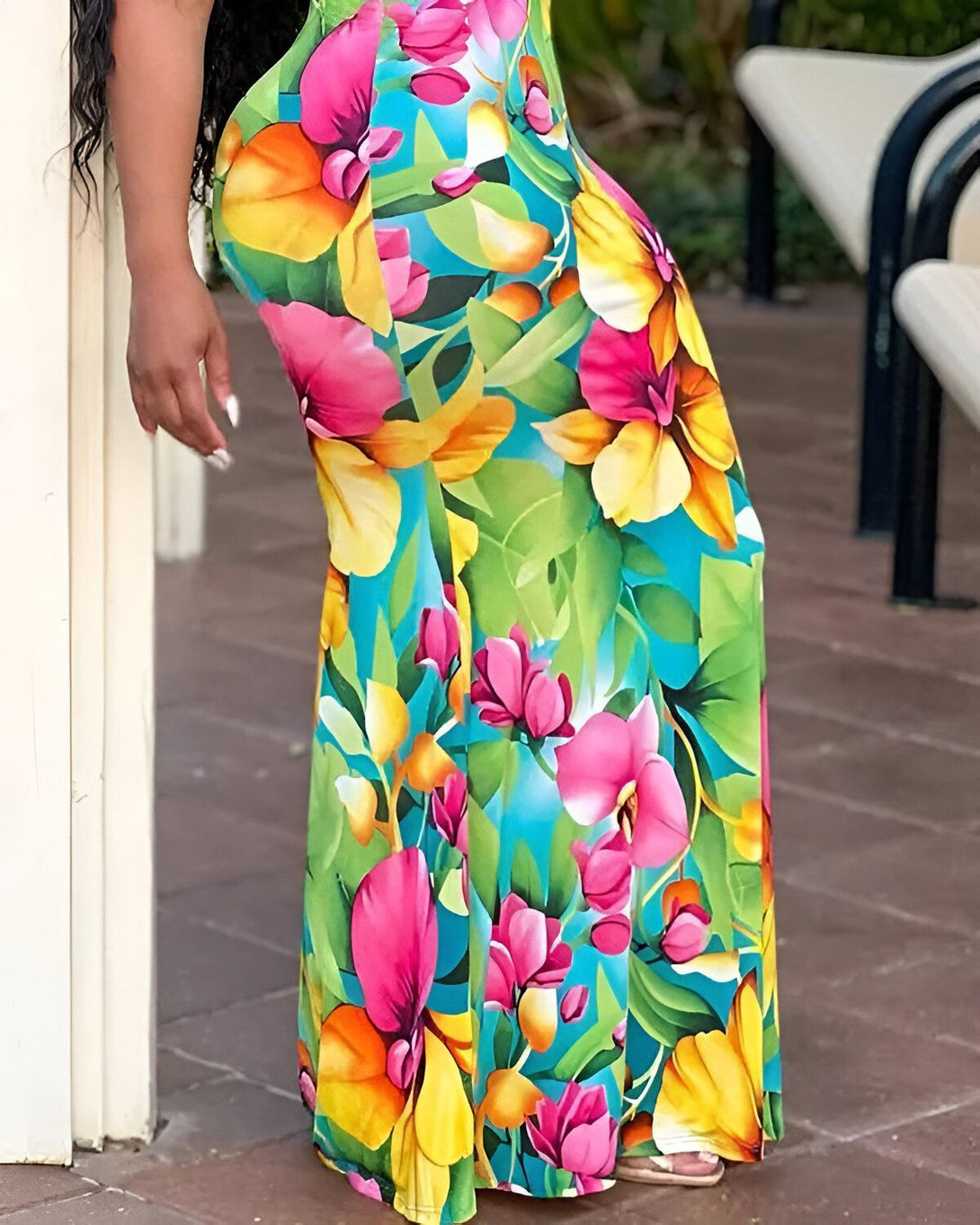Une femme porte une longue robe colorée à motifs floraux. Elle est debout près d'un mur blanc.