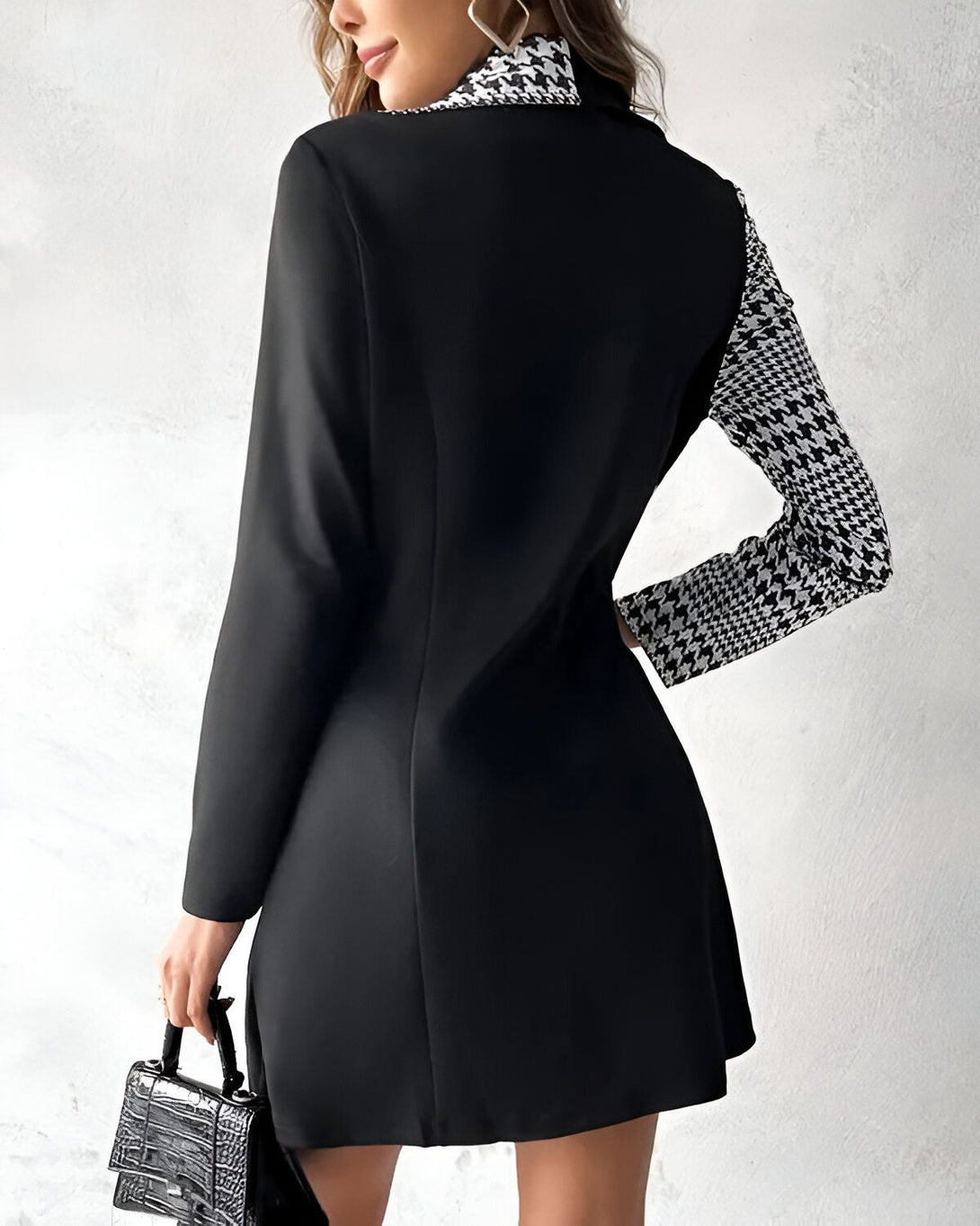 Une femme porte une veste noire et blanche. La veste est cintrée et a un col montant. La femme porte également un sac à main noir.