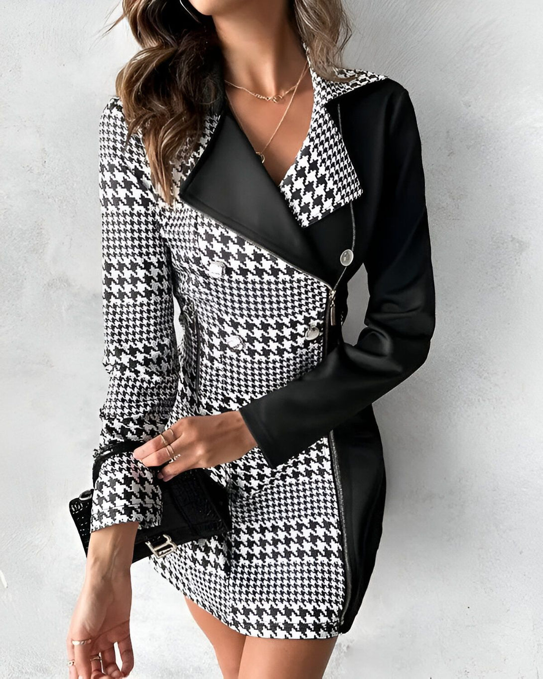Une femme porte une robe noire et blanche à motif pied-de-poule. La robe est cintrée à la taille et possède un col montant. Elle porte également un collier et un bracelet.