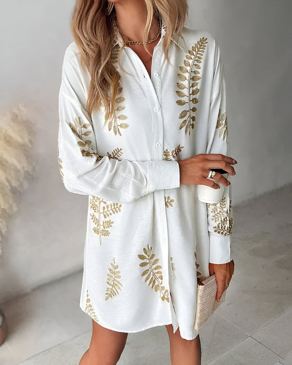 Une femme porte une chemise blanche à manches longues avec des feuilles dorées. Elle est ouverte et on peut voir un t-shirt blanc en dessous. Elle porte également un collier et un bracelet.