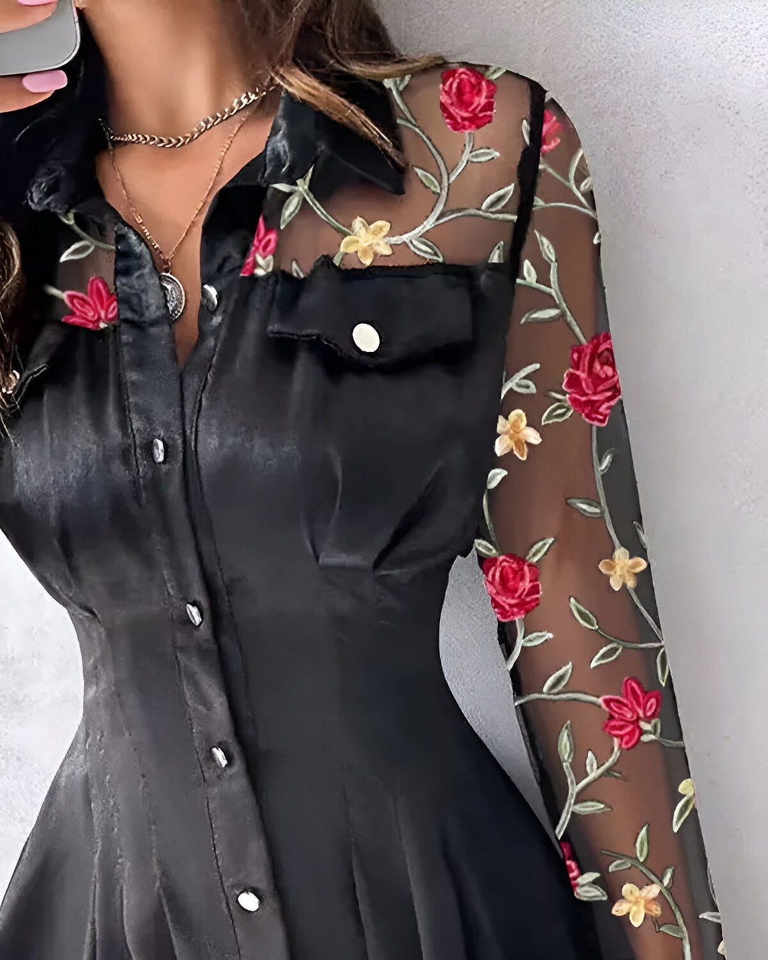 Une jeune femme porte une robe noire en satin avec des manches en mousseline brodées de fleurs rouges et jaunes.