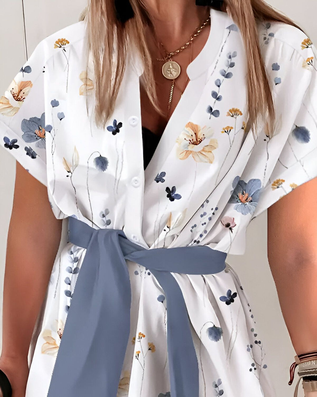 Une femme porte une robe blanche à fleurs bleues et jaunes. La robe est ceinturée d'un ruban bleu.