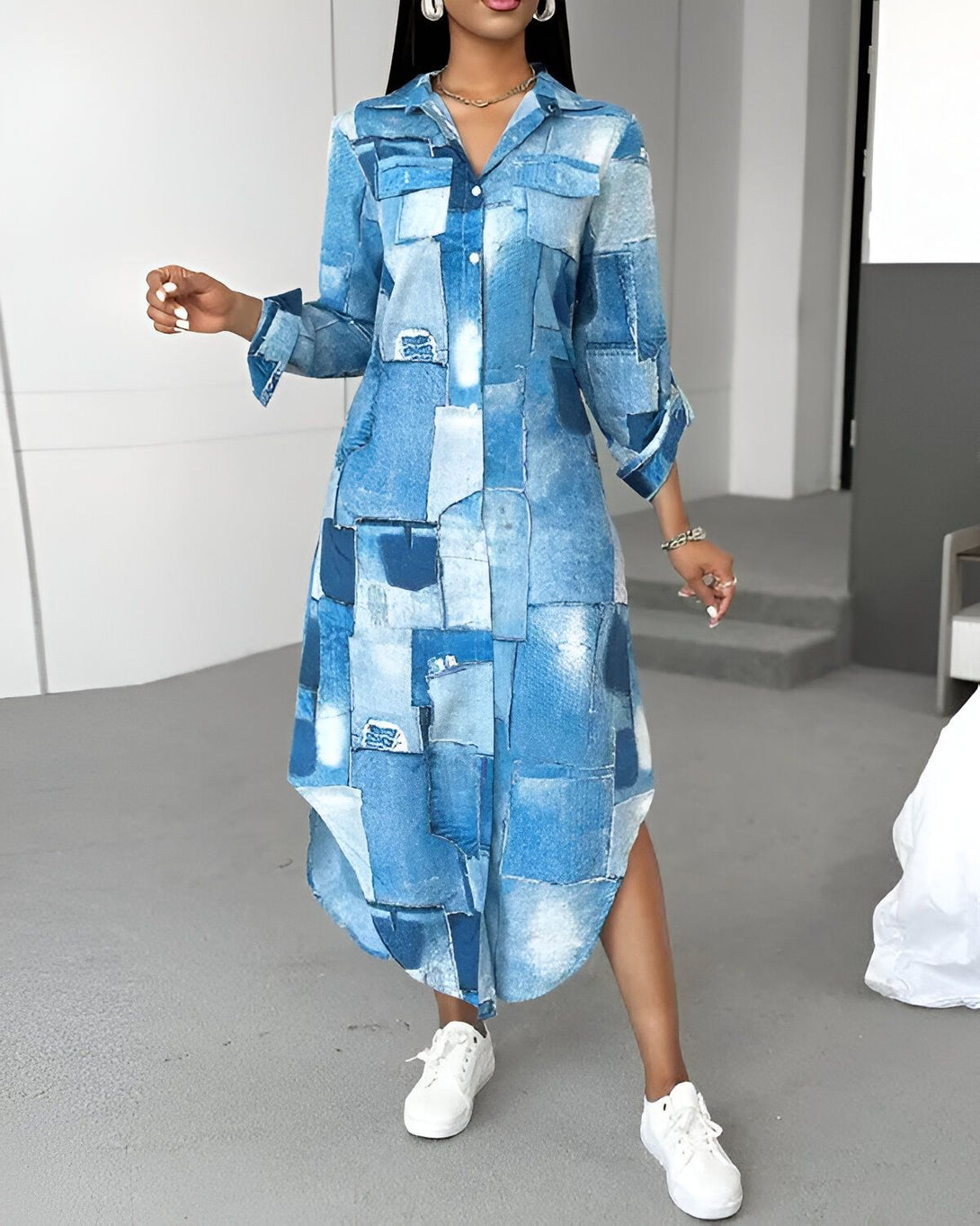 Une femme porte une robe chemise longue en patchwork. La robe est bleue et blanche. La femme est debout et porte des baskets blanches.