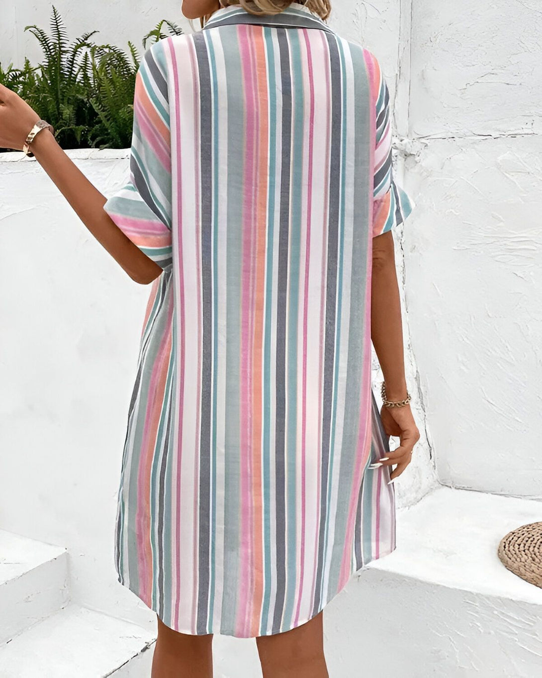 Une femme porte une robe chemise rayée multicolore. La robe est ample et a des manches courtes. La femme est vue de dos.