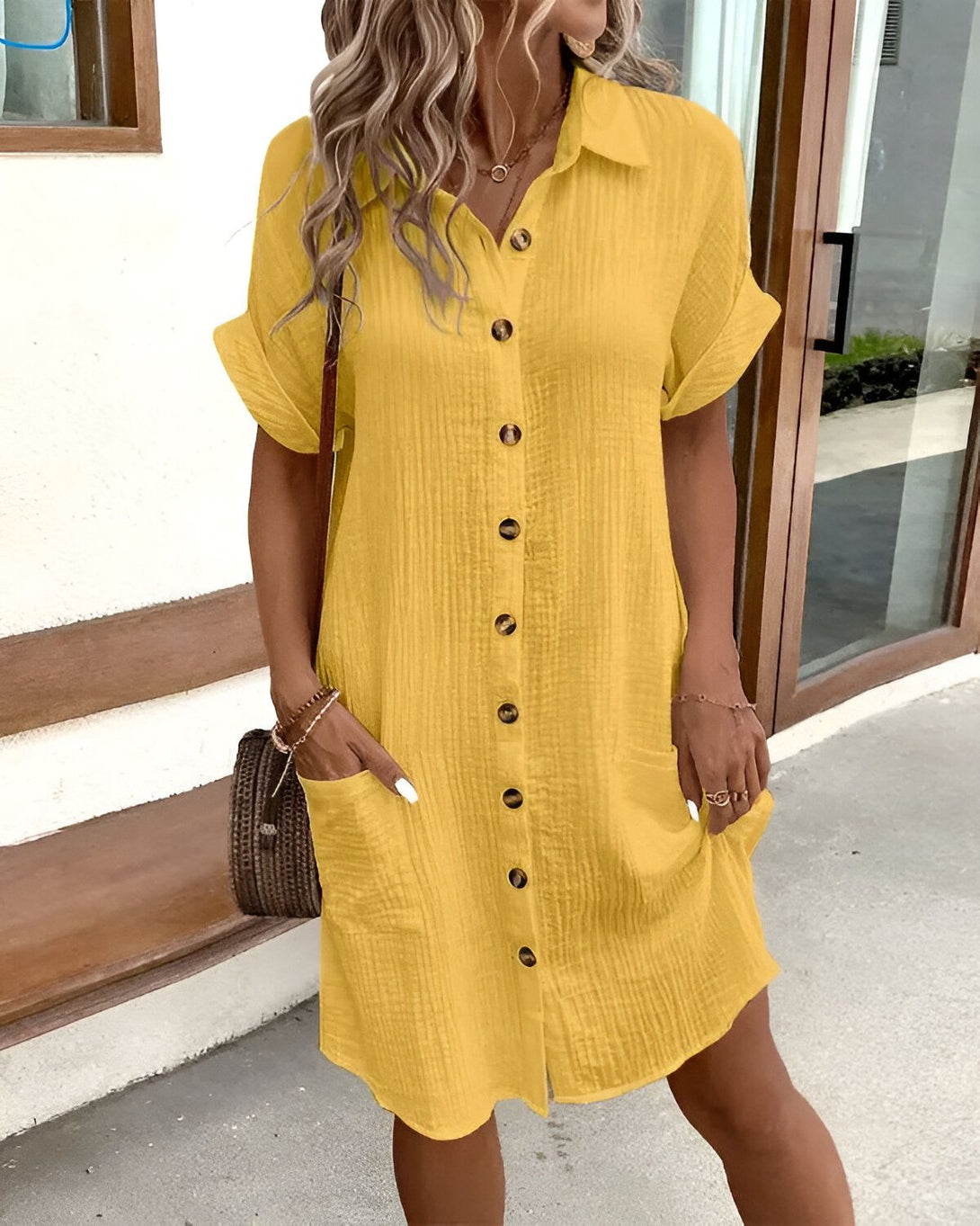 Une jeune femme porte une robe chemise jaune boutonnée. Elle a les cheveux longs et blonds. Elle est souriante et regarde l'appareil photo.