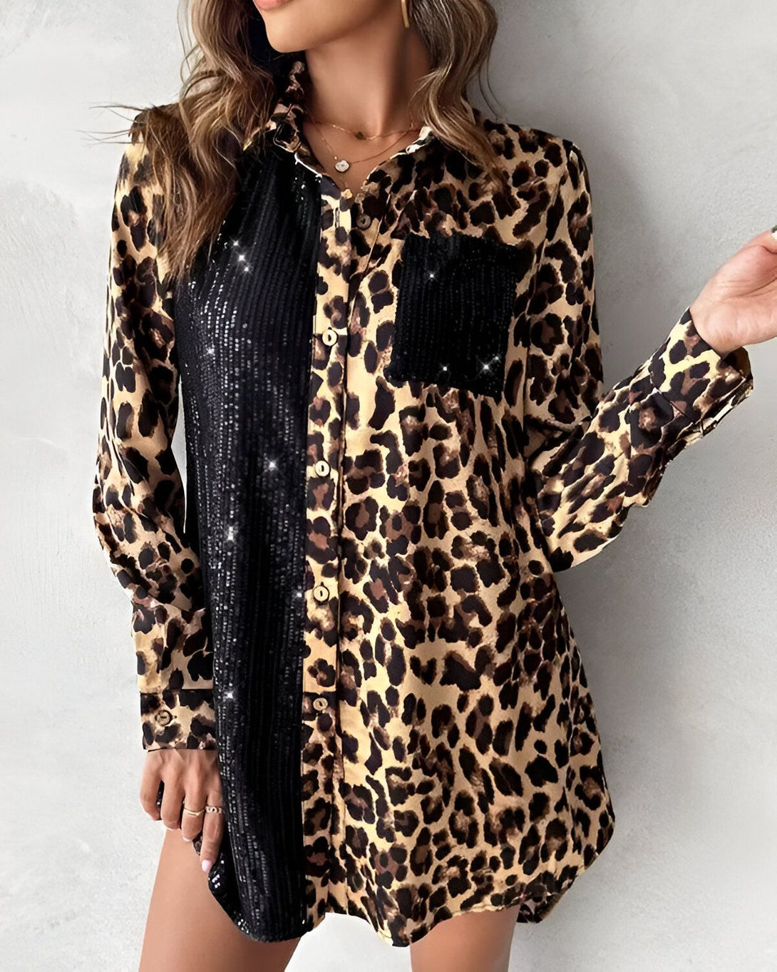Une femme porte une chemise léopard avec des sequins noirs. La chemise est ouverte et on peut voir un débardeur noir en dessous. La femme a les cheveux longs et bruns et elle porte un collier.