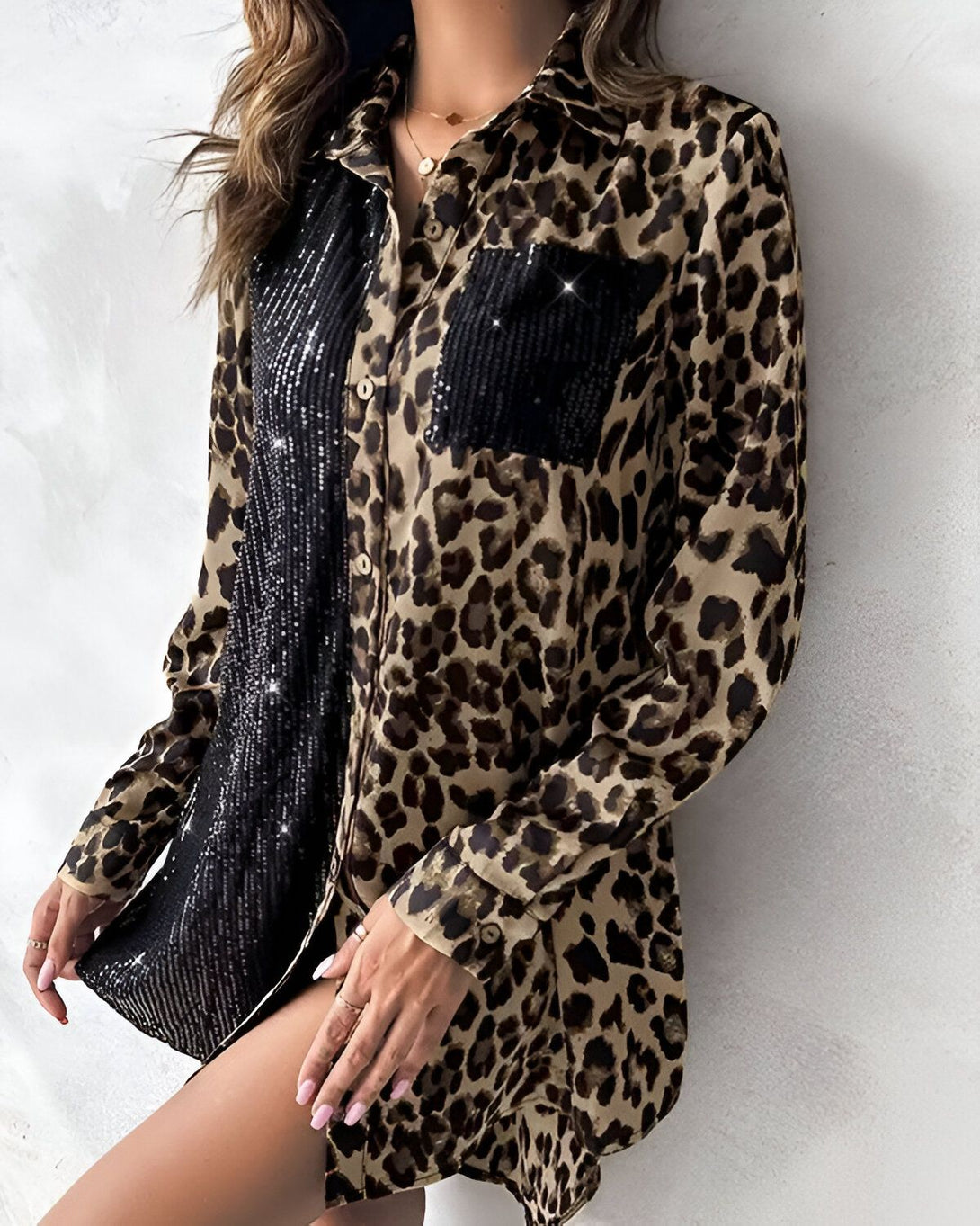 Une femme porte une chemise léopard avec des sequins noirs. La chemise est ouverte et on peut voir un short en dessous. La femme est debout et a une main sur la hanche. Elle a les cheveux longs et blonds et porte un collier.