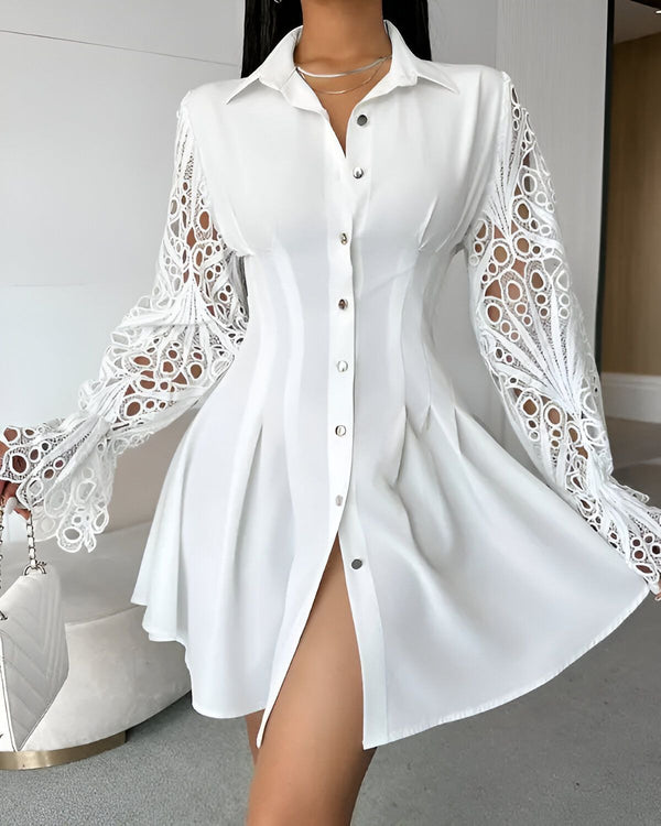 Une femme porte une robe chemise blanche. La robe est ouverte sur le devant et possède des manches longues et évasées. La femme est debout, les jambes écartées et les bras légèrement écartés du corps. Elle porte un collier et un sac à main blancs.