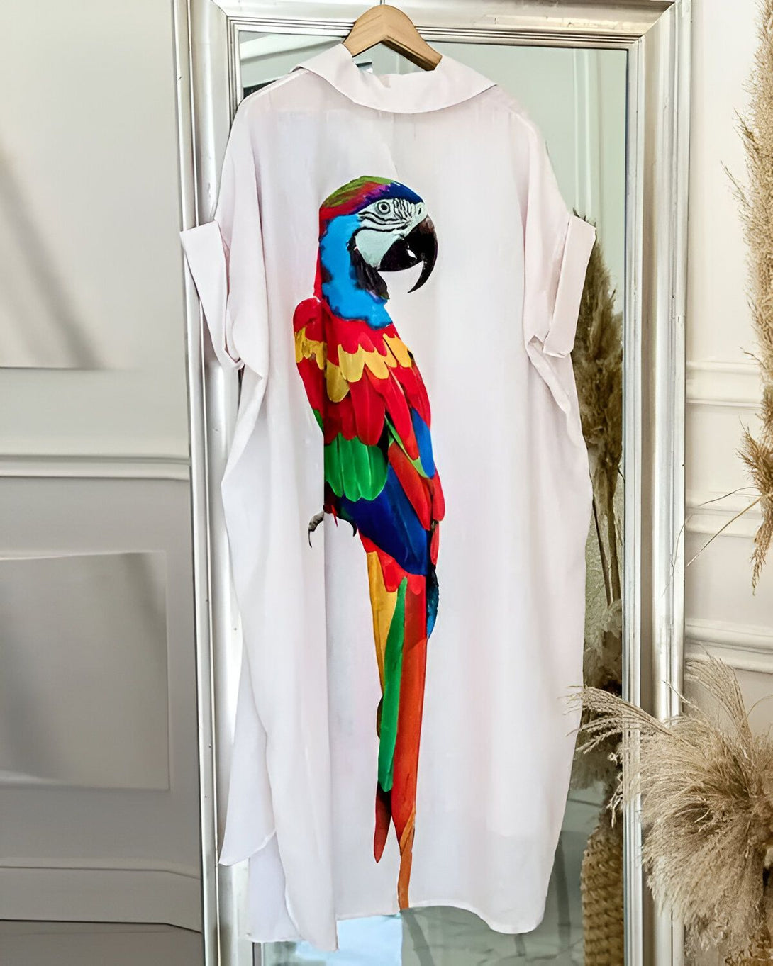 Une image d'une robe blanche avec un perroquet coloré imprimé dessus. Le perroquet est perché sur une branche et regarde vers la droite. La robe est mi-longue et a des manches courtes.