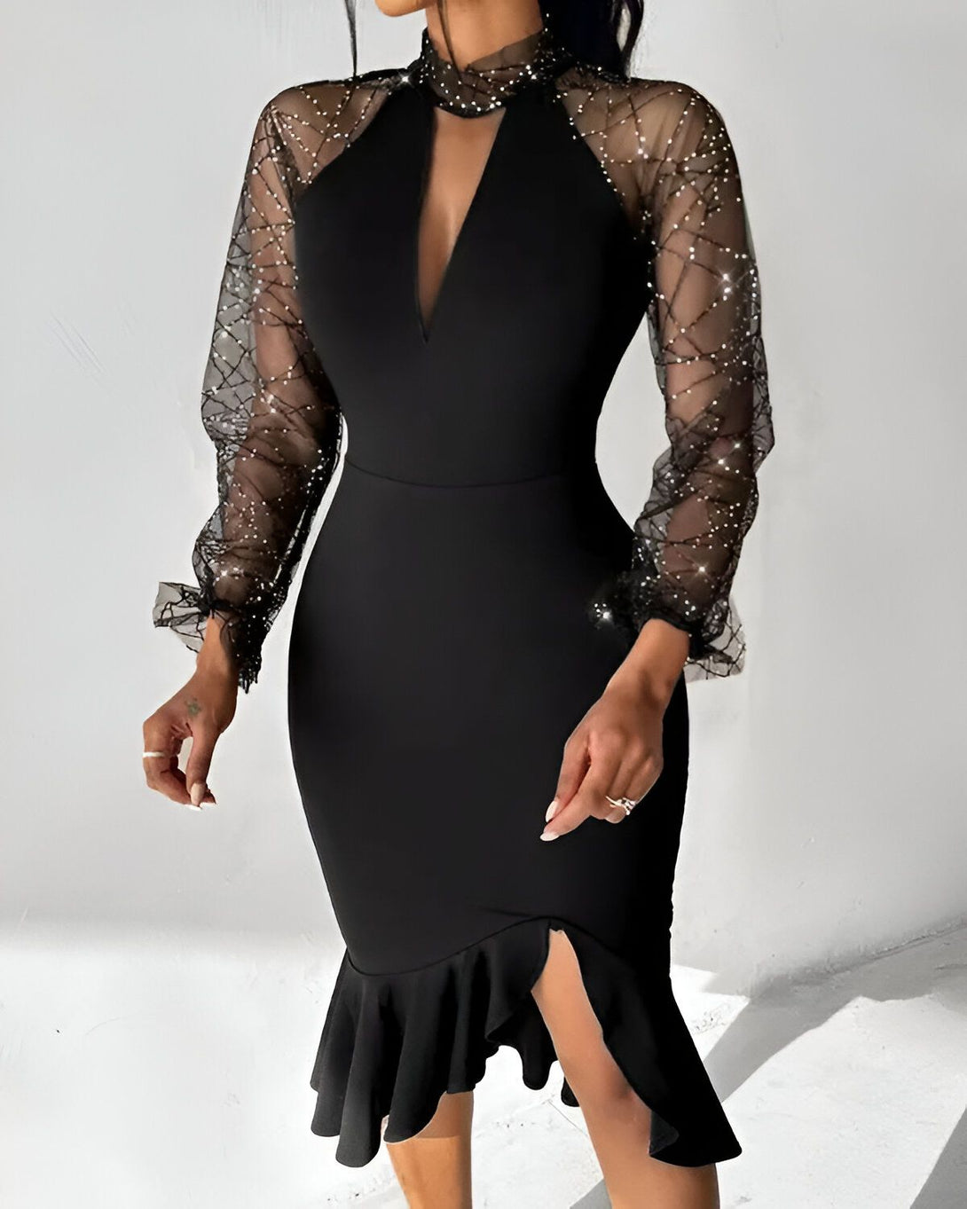 Une femme porte une robe noire moulante avec des manches en résille scintillantes. La robe a un col montant et une fente sur le côté.