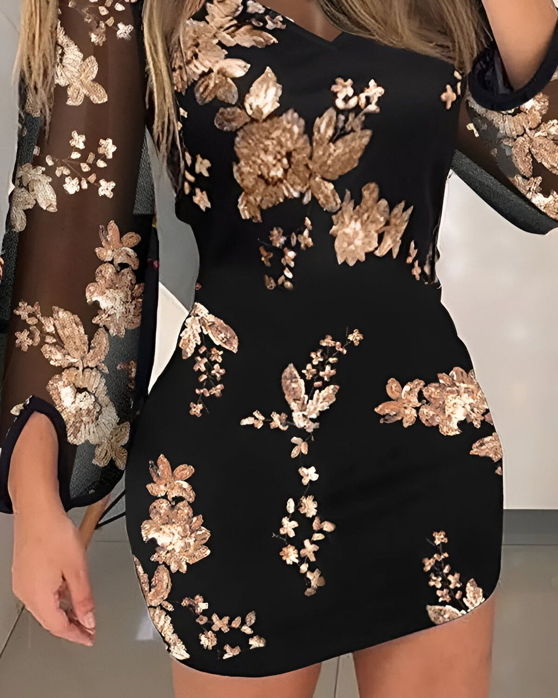 Une femme porte une robe noire moulante à manches longues. La robe est ornée de sequins dorés en forme de fleurs.