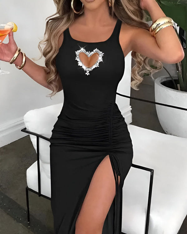 Une femme porte une robe noire moulante avec un décolleté en forme de cœur et une fente sur la jambe droite. Elle porte également des talons noirs et des bijoux.