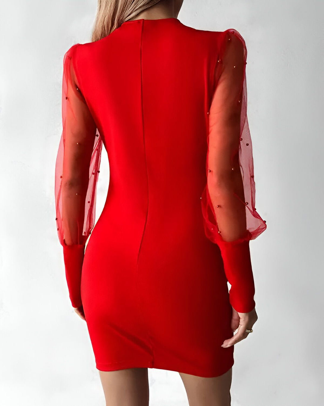 Une femme porte une robe rouge moulante avec des manches bouffantes en résille transparente parsemées de perles.