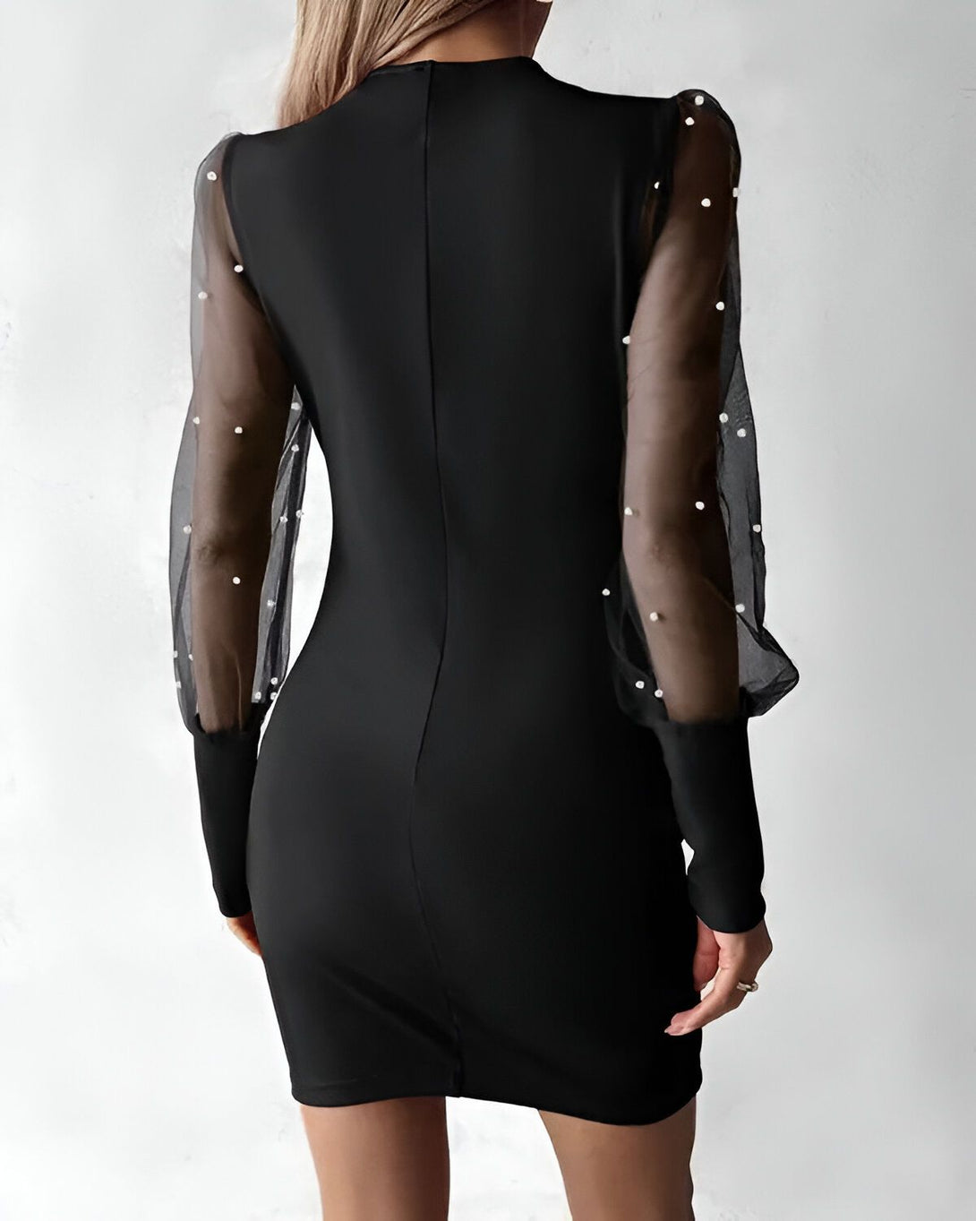 Une femme porte une robe noire moulante avec des manches bouffantes en résille transparente parsemées de perles blanches.