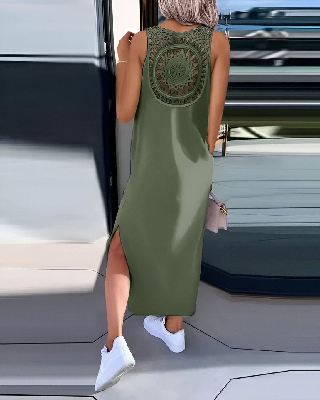 Une femme porte une robe longue vert kaki dos nu avec des motifs en dentelle. Elle est vue de dos et porte des baskets blanches.