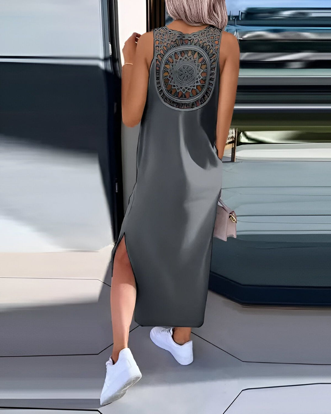 Une femme porte une robe longue grise avec un dos ajouré et desのスニーカー blanches.