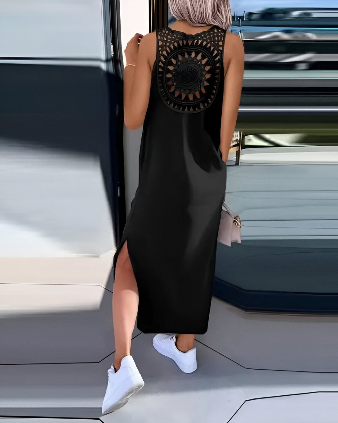 Une femme porte une robe noire longue avec un dos ajouré et desのスニーカー blanches.