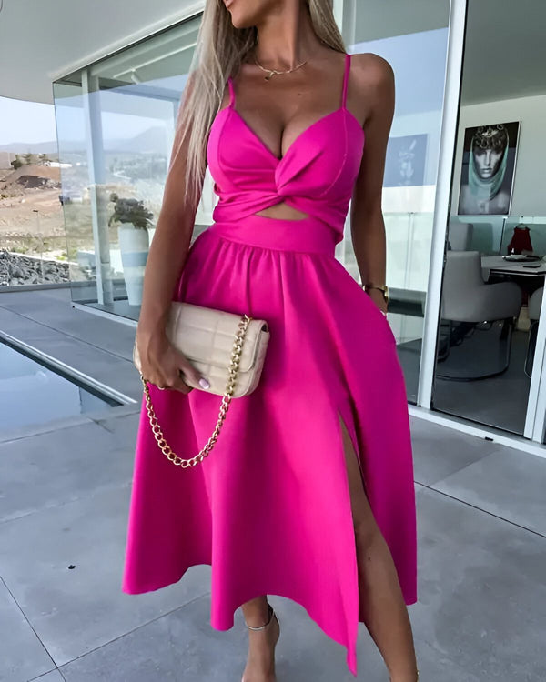 Une femme porte une robe rose fendue avec un décolleté plongeant et des bretelles fines. Elle porte également un sac à main beige et des talons hauts.