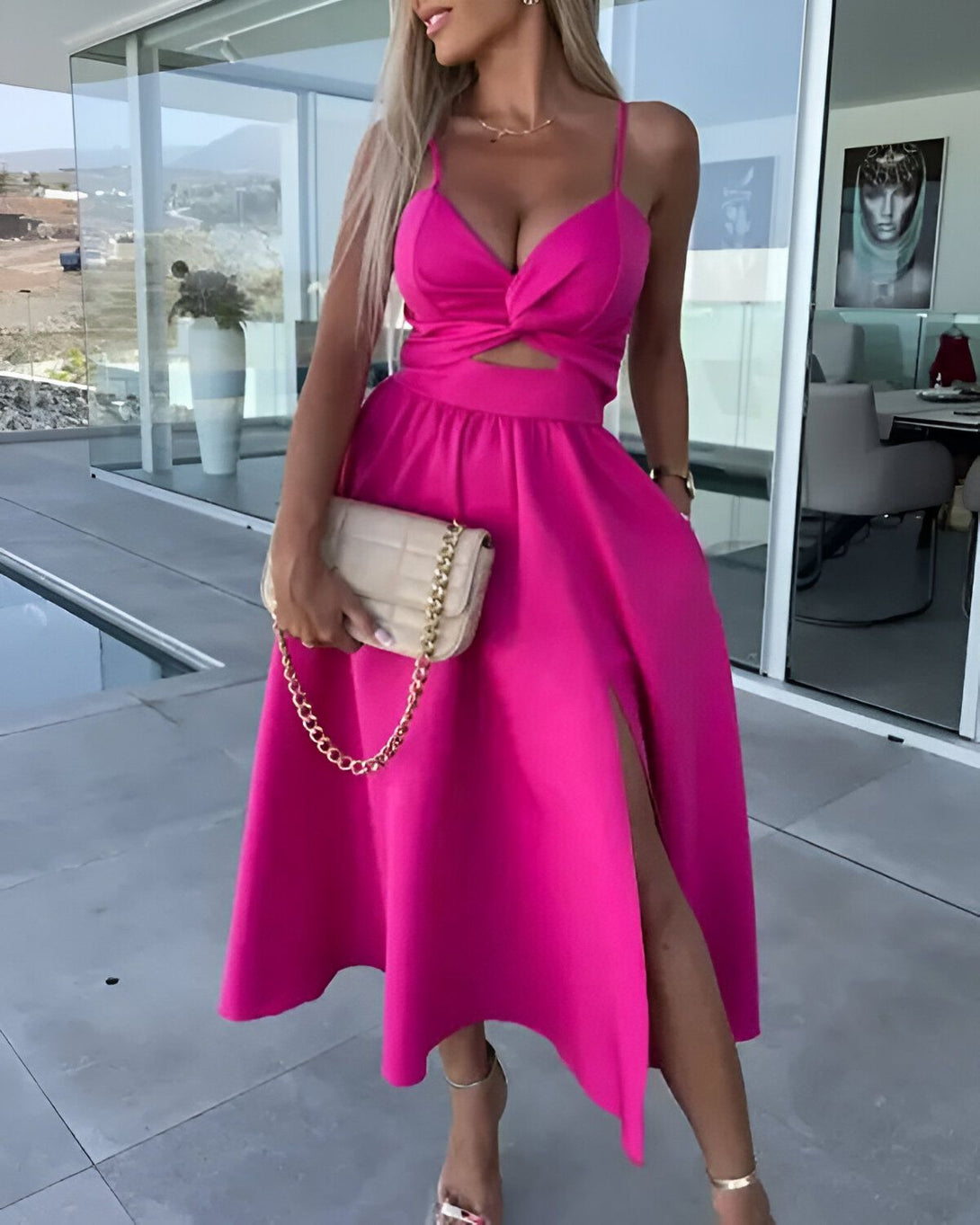 Une femme porte une robe rose fendue avec un décolleté plongeant. Elle porte également des talons hauts et un sac à main beige.