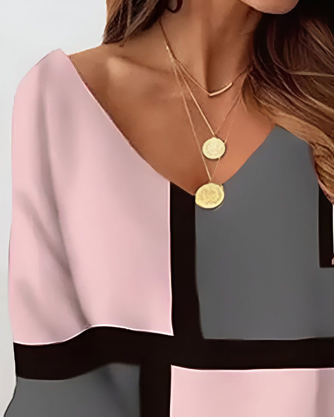 Une femme porte un chemisier rose et noir avec un décolleté en V. Le chemisier est fait d'un tissu léger et a des manches courtes. La femme porte également un collier avec un pendentif rond.