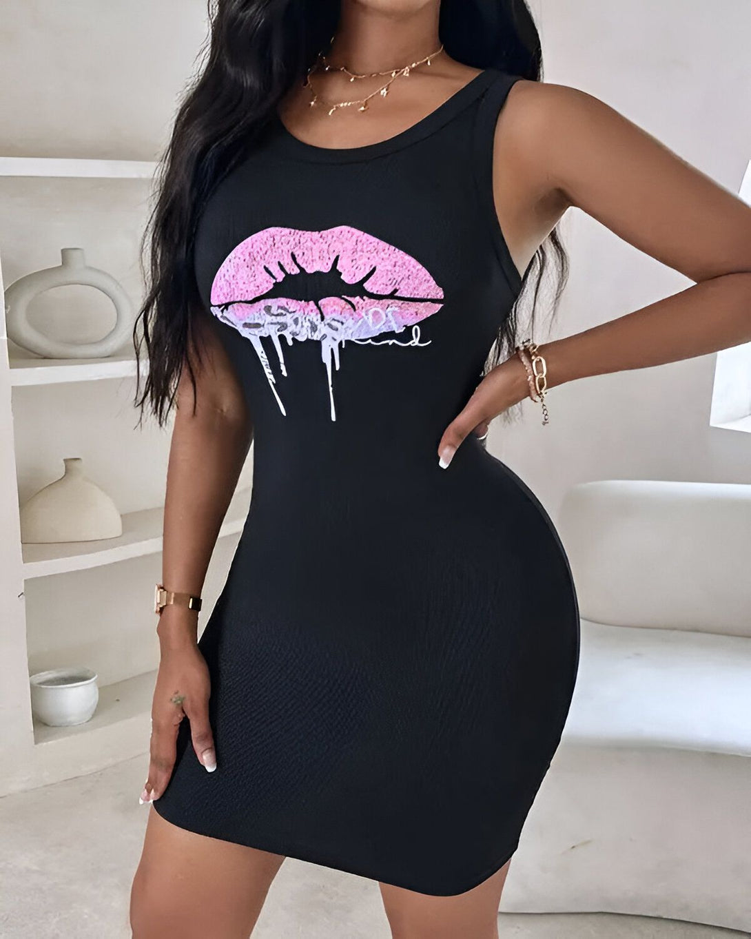 Une femme porte une robe noire moulante avec un imprimé lèvres roses. La robe est courte et sans manches. La femme est debout, les mains sur les hanches. Elle a les cheveux longs et noirs et porte un maquillage glamour.