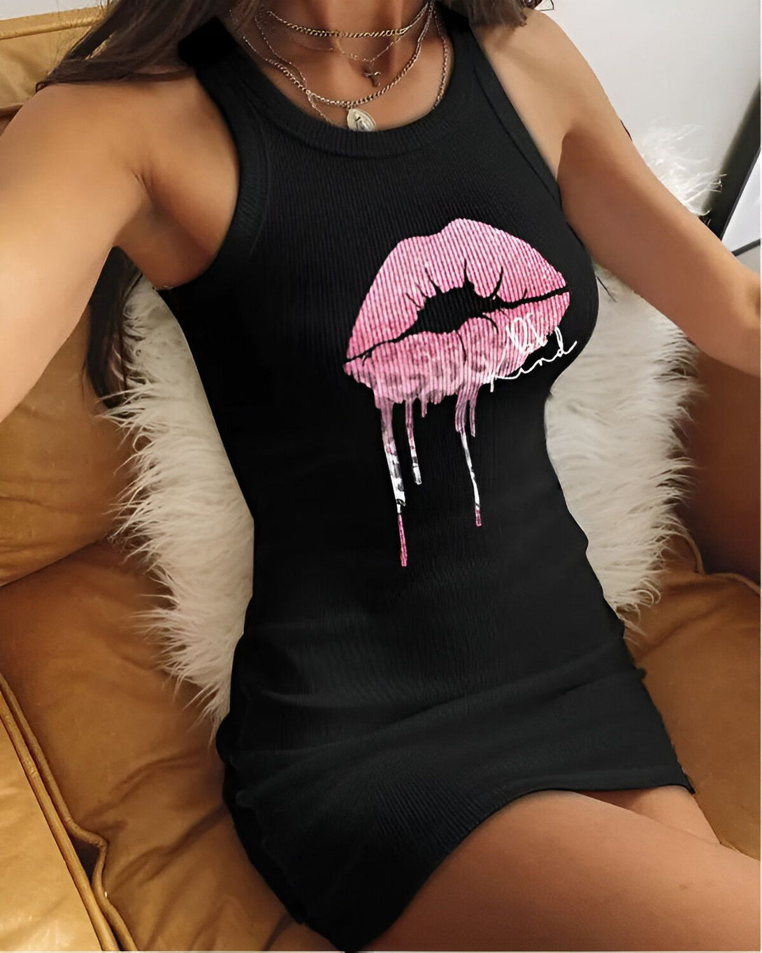 Une jeune femme porte une robe noire moulante avec un imprimé lèvres roses. La robe est courte et met en valeur ses jambes. Elle est assise sur un canapé et porte des talons hauts noirs.