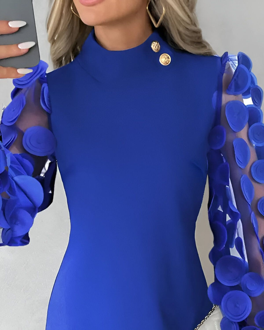 Une femme porte une robe bleue à manches longues. Les manches sont en mousseline de soie et comportent des détails floraux. La robe est cintrée à la taille et possède un col montant.