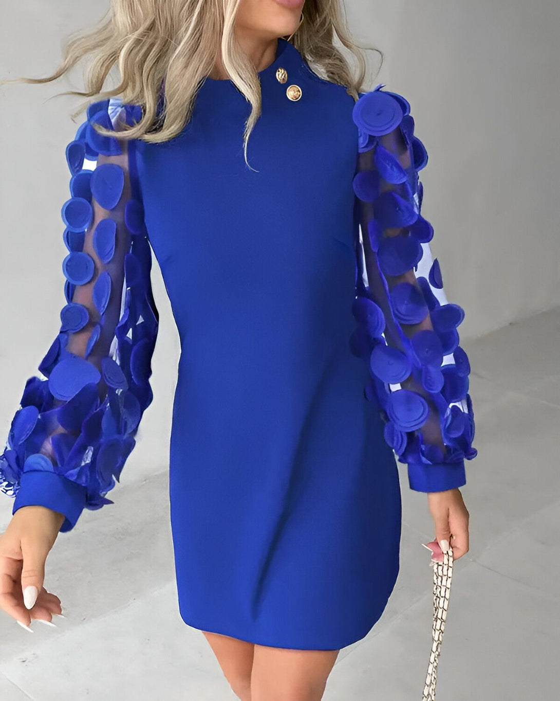 Une femme porte une robe bleue avec des manches bouffantes et des boutons dorés.