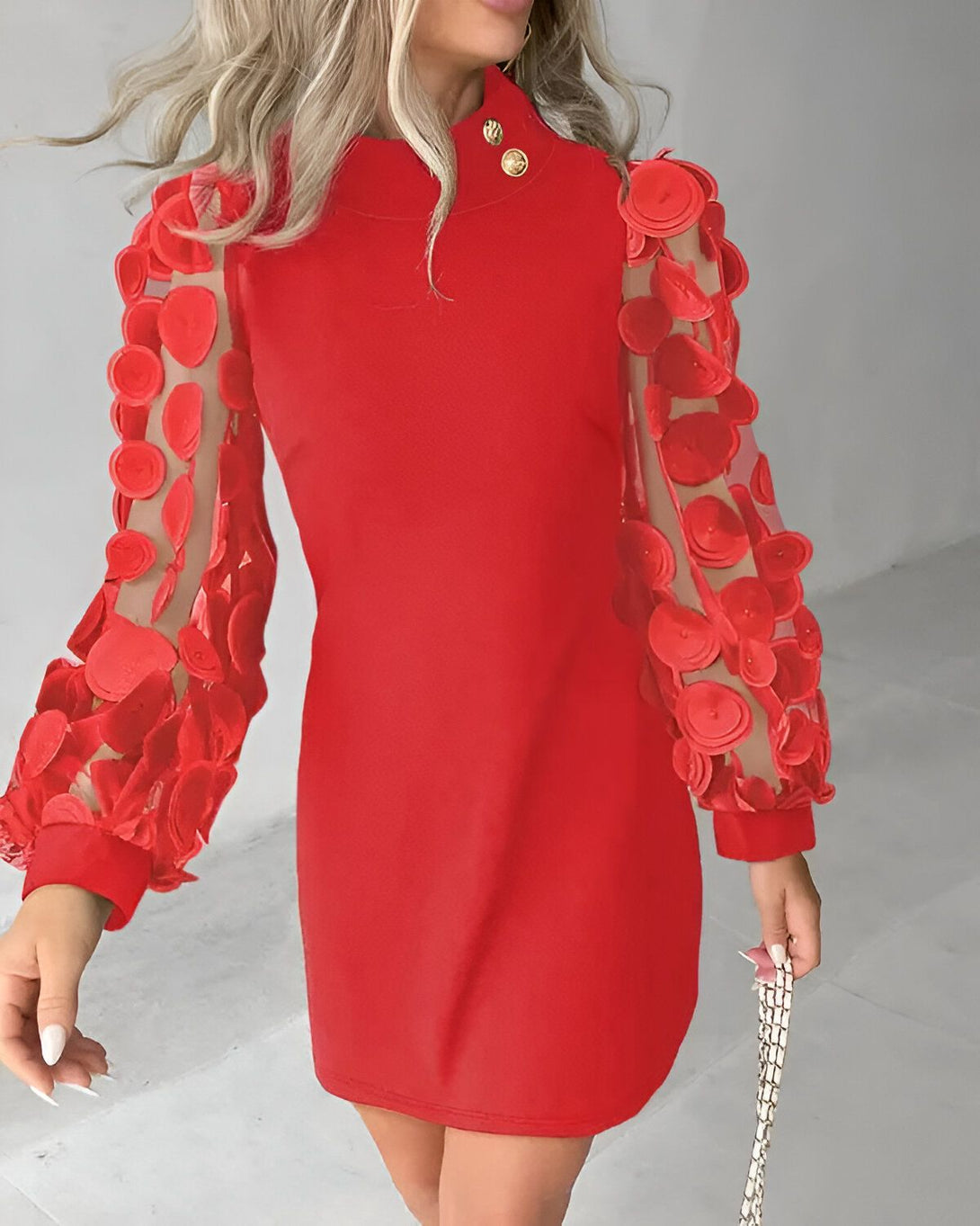 Une femme porte une robe rouge avec des manches bouffantes en résille et des boutons dorés.
