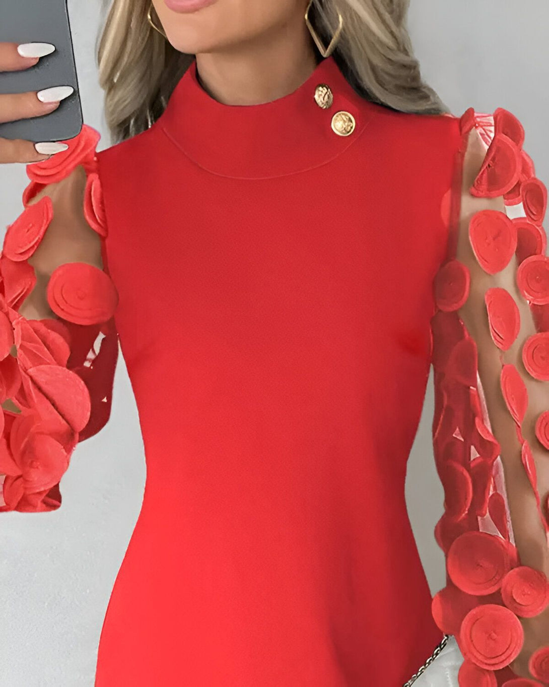 Une femme porte une robe rouge moulante à manches longues. La robe est encolure haute et possède des boutons dorés. Les manches sont transparentes et sont décorées de fleurs rouges en relief.